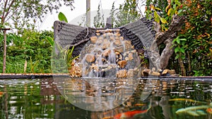 Fish pond with waterfall fountain. Garden waterfall landscaping with fishes, rocks, flowers and plants