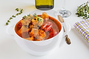 Fish soup with cod, tomato, onion, garlic and thyme in bowl on white table