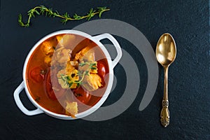 Fish soup with cod, tomato, onion, garlic and thyme in white bowl on black stone background, top view