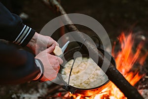 Fish soup cooking on fire in nature and the human hands cut potatoes in a pan.