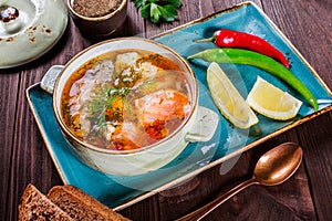 Fish soup with salmon and shrimps, dill, potatoes, lemon, peppers and bread on dark wooden background,