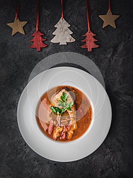 Fish soup in white plate and christmas decoration. Dark background. Overhead