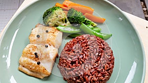 fish steak with brown rice and vegetables in green plate