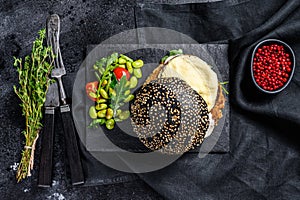 FishBurger with black brioche bun, omelette, fish cutlet and arugula. Black background. Top view photo