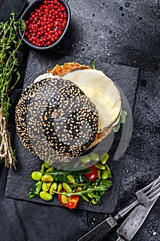 FishBurger with black brioche bun, omelette, fish cutlet and arugula. Black background. Top view photo