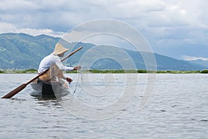 Fisheerman fishing ans sitting on small wooden boat on inle lake in myanmar
