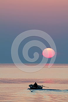 Fisher boat in sunset on the horizon above sea