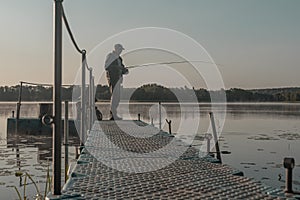 Fisher fishing in foggy morning. Man with fish rod resting on lake in mist