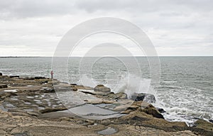 Fisher fishing in Mardel Plata coast Sea and gray sky , Breaking waves on the rocks photo