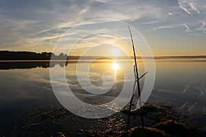 Fisher man fishing with spinning rod on a river bank at misty foggy sunrise