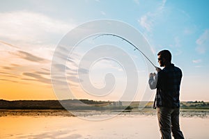 Fisher man fishing with spinning rod on a river bank at misty foggy sunrise. fisher with spinning. spinning concept.