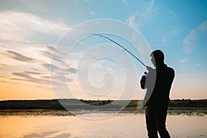 Fisher man fishing with spinning rod on a river bank at misty foggy sunrise. fisher with spinning. spinning concept.