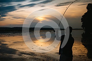 Fisher man fishing with spinning rod on a river bank at misty foggy sunrise. fisher with spinning. spinning concept.