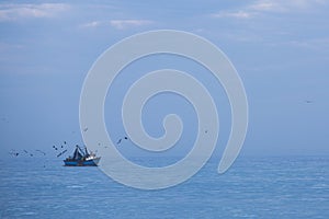 Fisher ship, blue Pacific Ocean and many birds flying over, Peru