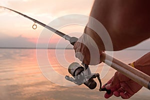 Fisher's hands holding reel, fishing at the sunset