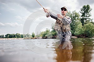 Fisherman in action. Guy is throwing spoon of fly rod in water and holding part of it in hand. He looks straight forward