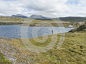 Fisherman, angler figure at northern landscape, tundra in Swedish Lapland with blue artic lake, green hills and