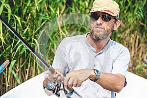 Fisherman with beard sitting in boat and holding fishing rod