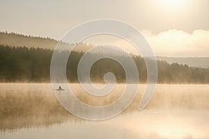 A fisherman in a boat catches fish in the early foggy morning