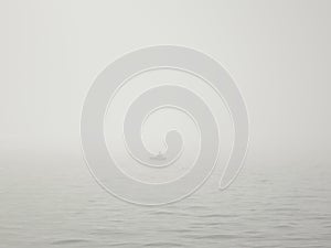 Fisherman in a boat on a lake in a thick fog catches fish with a fishing rod