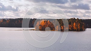 Fisherman in a boat near a small island on the lake. Autumn forest, distant panorama