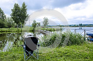 A fisherman in a cap sits in a chair near the lake with a fishing rod and catches fish