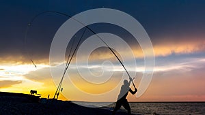 Fisherman cast fishing rods on the seashore at a dramatic sunset. Fisherman silhouette. Night fishing with illuminated