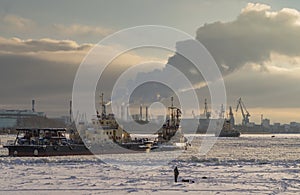 A fisherman catches fish on a frozen river and looks at the ships. Winter navigation on the river. Ice fishing