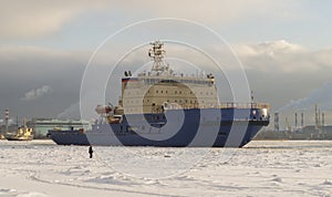 A fisherman catches fish on a frozen river and looks at the ships. Winter navigation on the river. Ice fishing