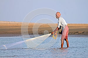 A fisherman catches fish by traditional hand net in India