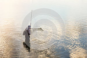 A fisherman catches fish using a fishnet on tranquil lake