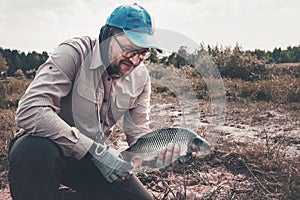 Fisherman caught and holds a carp in his hands