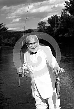 Fisherman caught a trout fish. Portrait of cheerful senior man fishing. Grandfather with catch fish. Mature man