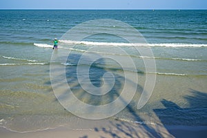 Fisherman in colorful shirt and pants waiting for fishing on the beach with soft sea wave, coconut tree shadow and blue sky