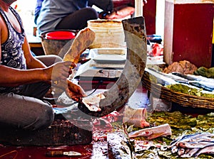 Fisherman cutting fish on a standing blade boti with the help of a wooden stump in indian fish market at kolkata