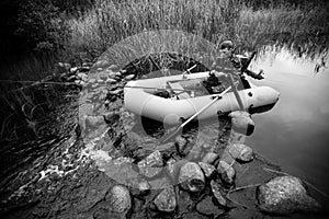 Fisherman dressed in camouflage fishing in the river with a rubber boat. Black and white photo.