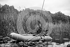 A fisherman dressed in camouflage fishing in the river with a rubber boat. Black and white photo.