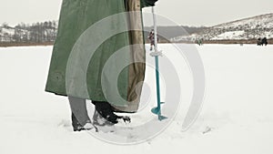 Fisherman drills ice hole on frozen river. Man with ice drill in hands is drilling ice hole. Winter fishing concept