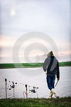 Fisherman at the edge of the lake looking at the fishing rods