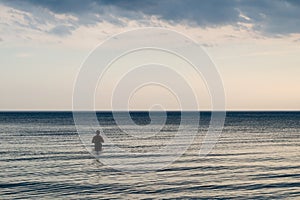 Fisherman entered the waters of the sea on the background of the purple - gray - blue cloudy sky