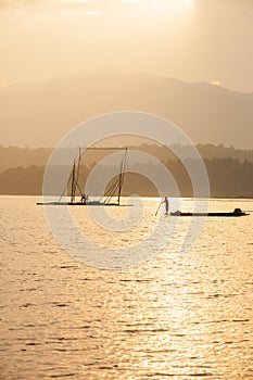 Fisherman on fishing boat in The Sirikit Dam, raft dip net and sunset sky backgrounds. Golden sun setting shines down around the