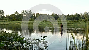 Fisherman fishing in a calm river in the morning. Man in fishing gear stending in a river and throws a fishing pole