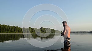 Fisherman fishing in a calm river in the morning. Man in fishing gear stending in a river and throws a fishing pole