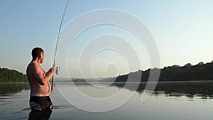 Fisherman fishing in a calm river in the morning. Man in fishing gear stending in a river and throws a fishing pole
