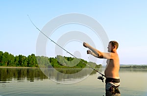 Fisherman fishing in a calm river in the morning. Man in fishing gear stending in a river and throws a fishing pole