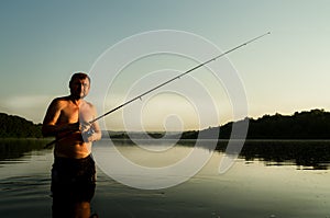 Fisherman fishing in a calm river in the morning. Man in fishing gear stending in a river and throws a fishing pole