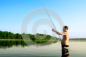 Fisherman fishing in a calm river in the morning. Man in fishing gear stending in a river and throws a fishing pole