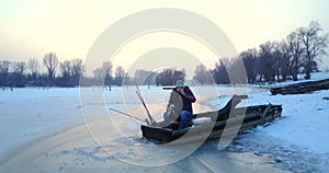 Fisherman fishing from hole in lake from his boat at winter