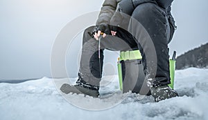 Fisherman is fishing in a hole on a large frozen lake on a sunny day. The joy of winter fishing