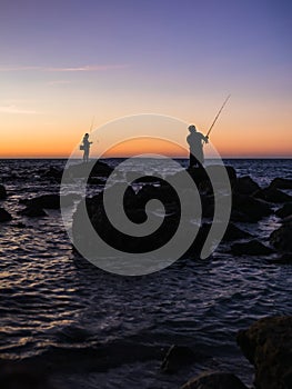 Fisherman fishing from rocks at sunset